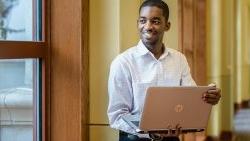 Student standing while holding laptop computer